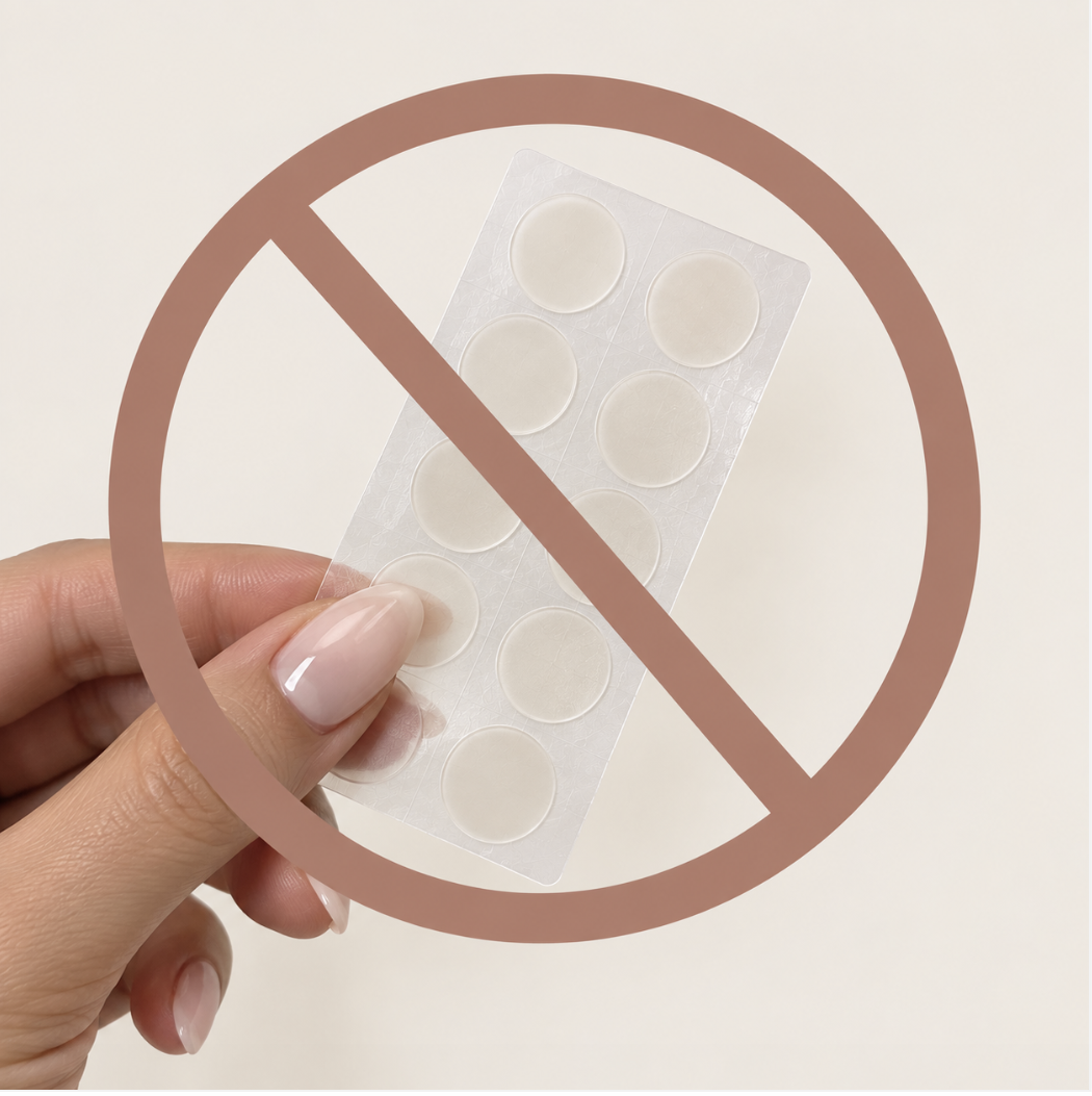 A sheet of round hydrocolloid pimple patches beside a folded towel and gentle cleanser on a warm cream background